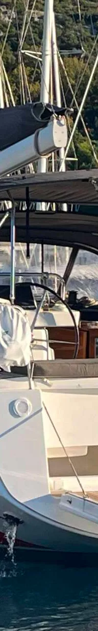 Een zeilboot met de naam "NOTUS" ligt in het water, met een persoon aan het roer en andere boten op de achtergrond.