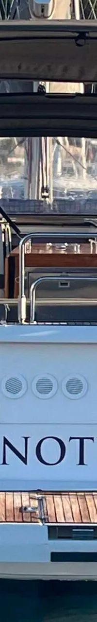 Een witte zeilboot met de naam "NOTUS" op de spiegel, met een man aan het stuur en een open zwemplateau.