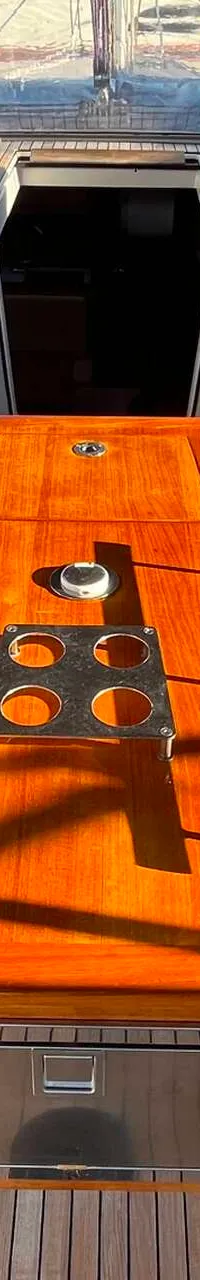 Een houten tafel met een ingebouwde koelkast en bekerhouders staat in de kuip van een boot. — Dufour 520 Grand Large