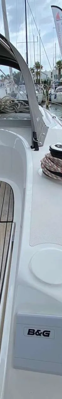 Een deel van een witte boot met een houten dek en een grijze kap, liggend in een haven naast een donkerblauwe boot.
