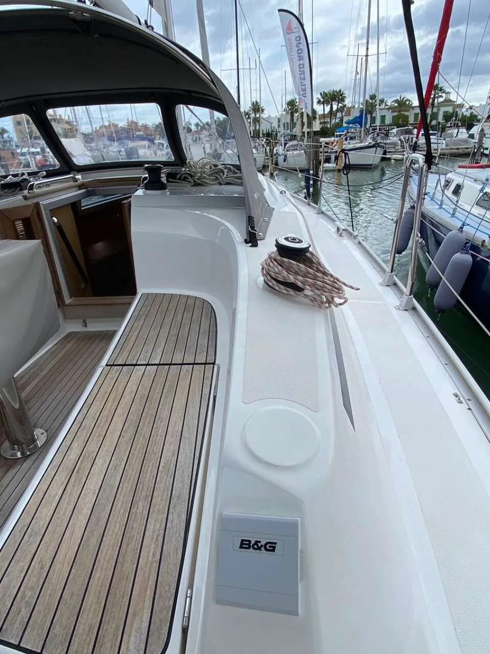 Een deel van een witte boot met een houten dek en een grijze kap, liggend in een haven naast een donkerblauwe boot.