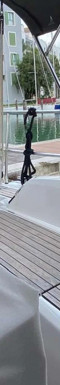 Een boot met een teakdek en afdekhoezen ligt in een jachthaven met gebouwen en palmbomen op de achtergrond.