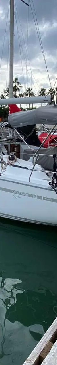 Een witte zeilboot met grijze bimini en buiskap ligt afgemeerd aan een houten steiger in een haven. — Bavaria 34 Cruiser