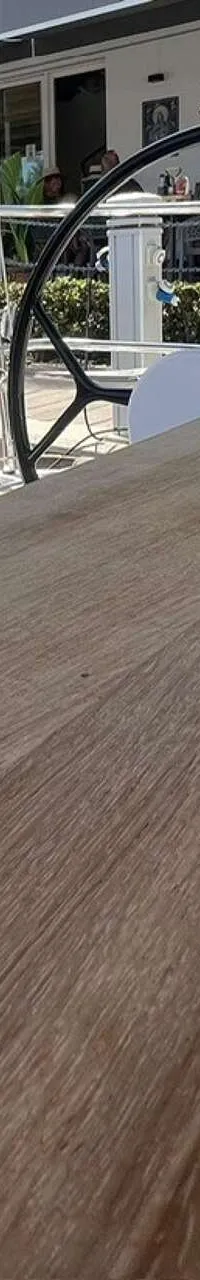 Een houten dek met een zwart stuurwiel en een gebouw met mensen op de achtergrond.