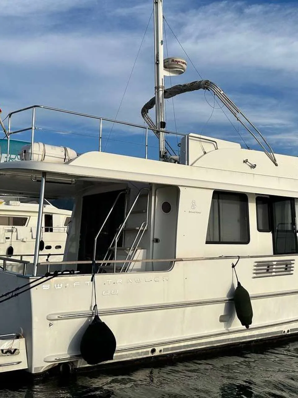Een witte motorboot met de tekst "SWIFT TRAWLER 44" op de zijkant ligt aangemeerd in een haven. — Beneteau Swift Trawler 44