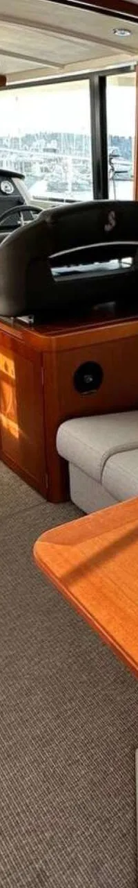 De foto toont het interieur van een boot met een stuurstand, een zithoek met tafel, en een kleine kombuis.