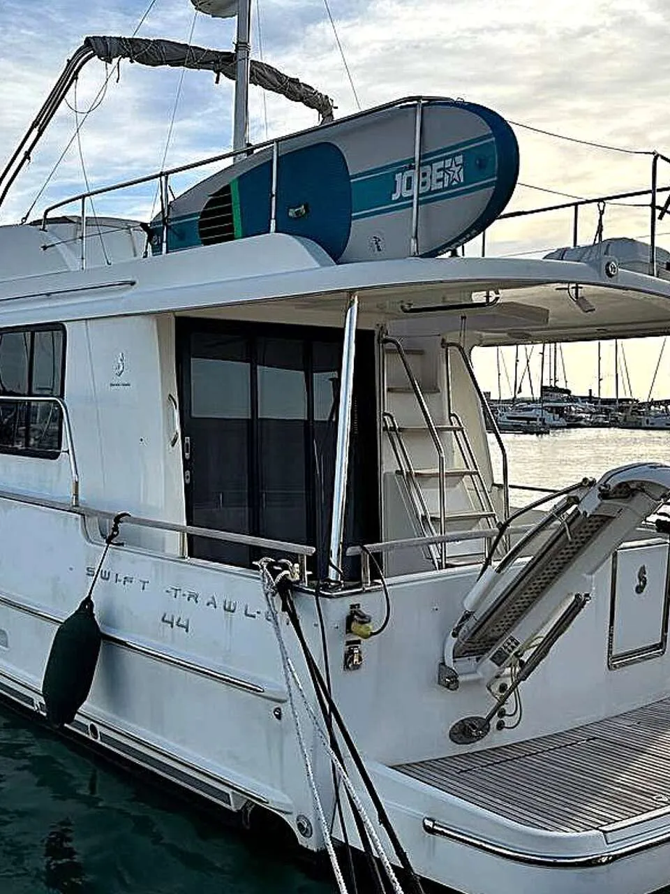 Een witte boot met de tekst "SWIFT TRAWLER 44" op de zijkant ligt aangemeerd in een haven. — Beneteau Swift Trawler 44