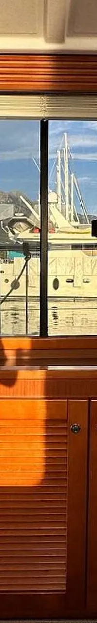Een interieur van een boot met houten kasten, een raam met uitzicht op een haven en een aanrecht met spoelbak.