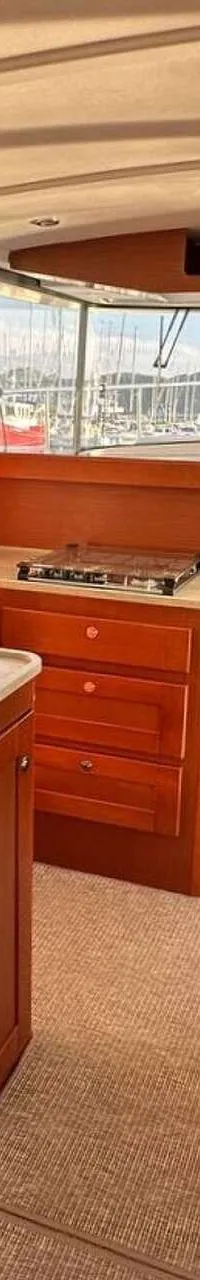 De foto toont het interieur van een boot met een kombuis, stuurstand en uitzicht op een haven vol boten.