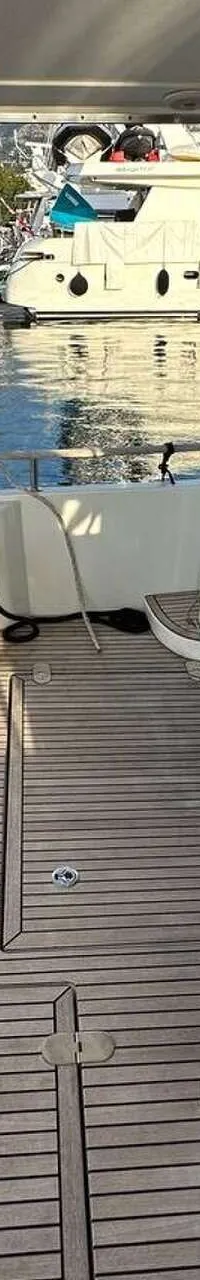 De foto toont een teakdek met een bankje, een trap en een loopplank naar de kade, met bergen op de achtergrond.