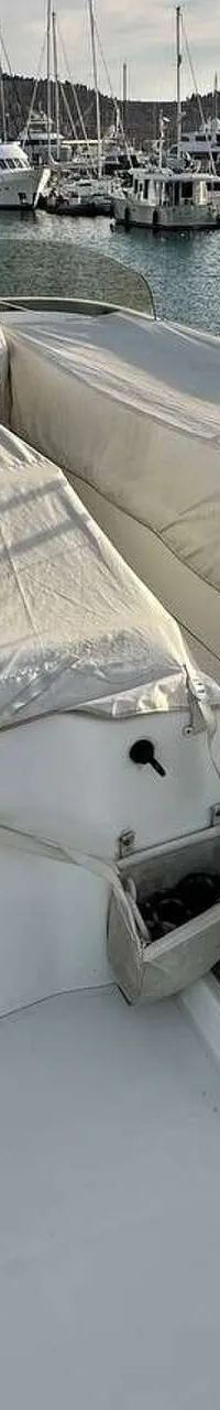 Een wit dek met twee afgedekte zitbanken en een mast, met op de achtergrond een jachthaven vol boten.