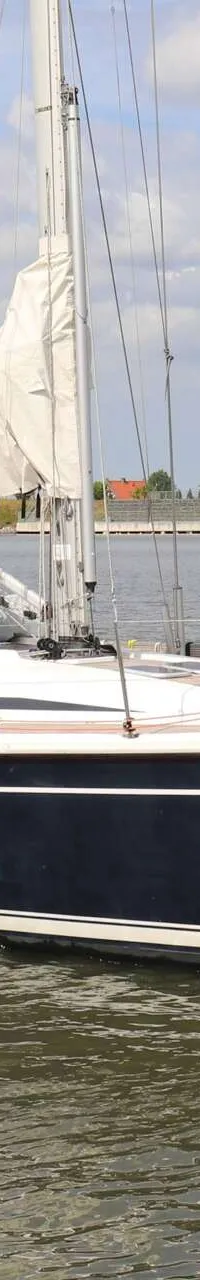 Een donkerblauwe zeilboot met witte strepen en een witte opbouw vaart op een waterweg. — Dehler 39 SQ
