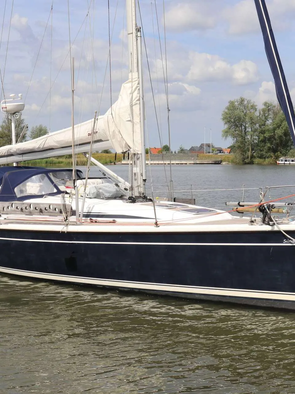 Een donkerblauwe zeilboot met witte strepen en een witte opbouw vaart op een waterweg. — Dehler 39 SQ