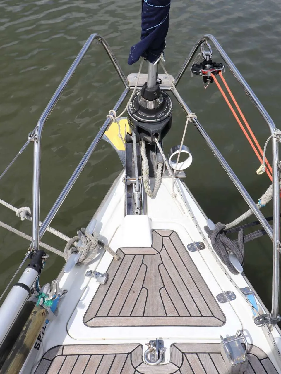 De foto toont de boeg van een zeilboot met een teakdek, reling, een opgerold zeil en diverse lijnen. — Dehler 39 SQ