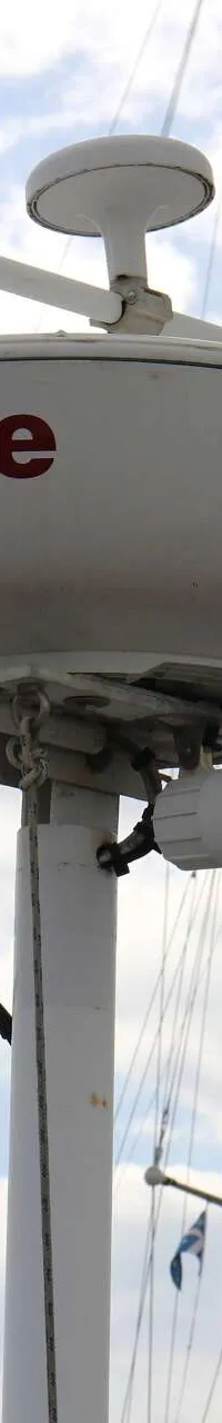 Een witte Raymarine radarbol met een luidspreker en antennes is gemonteerd op een mast, met andere masten op de achtergrond.