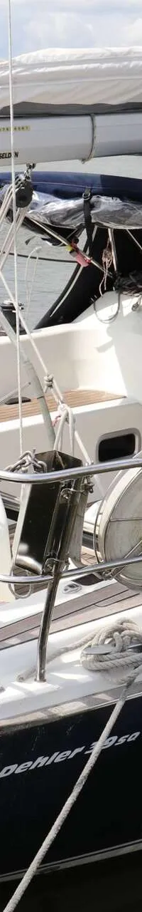 Een blauw-witte zeilboot met houten dek ligt aangemeerd, met een blauwe buiskap en stootwillen aan de zijkant. — Dehler 39 SQ