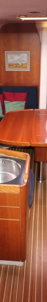 De foto toont het interieur van een boot met een kombuis, zithoek, tafel en een bed in de boeg. — Dehler 39 SQ