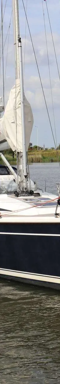 Een donkerblauwe zeilboot met witte strepen vaart op een waterweg met een man aan het roer. — Dehler 39 SQ
