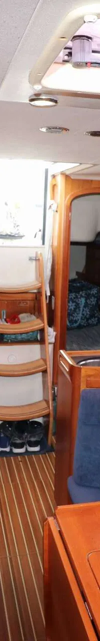 De foto toont het interieur van een boot met houten wanden, een kombuis, zithoeken en een trap naar de uitgang.