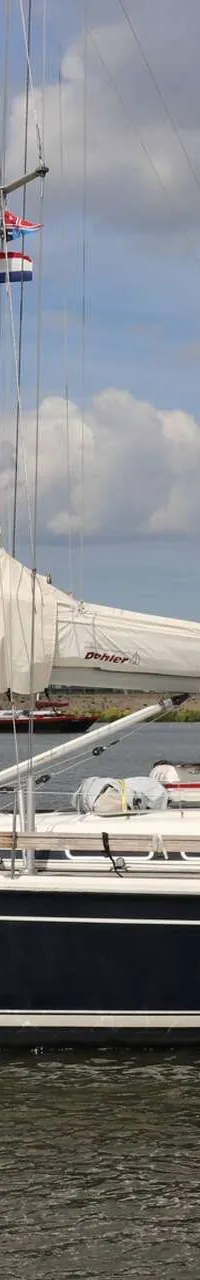 Een donkerblauwe zeilboot met witte strepen vaart op het water, met een man aan het roer en een zeil met "Dehler" erop.