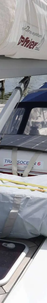 Een zeilboot met een blauwe buiskap, een opgevouwen zeil, een zonnepaneel en een reddingsvlot, ligt aangemeerd aan een…