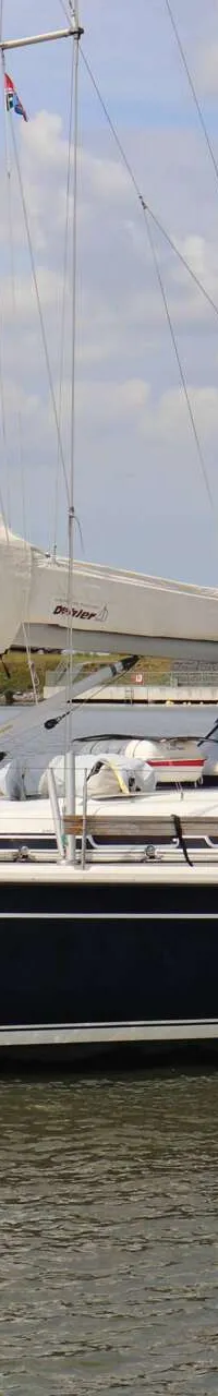Een donkerblauwe zeilboot met witte strepen op de romp vaart op een waterweg met bomen op de achtergrond. — Dehler 39 SQ