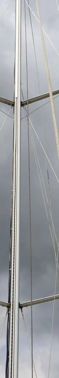 Een mast met verstaging en zalingen, met daaronder een Nederlandse en een Britse vlag, tegen een bewolkte lucht.