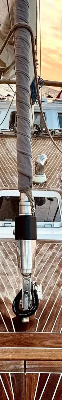 Een zeilboot met een houten dek vaart op zee, met een deels uitgerold zeil en een mast aan de voorzijde. — CRN 63