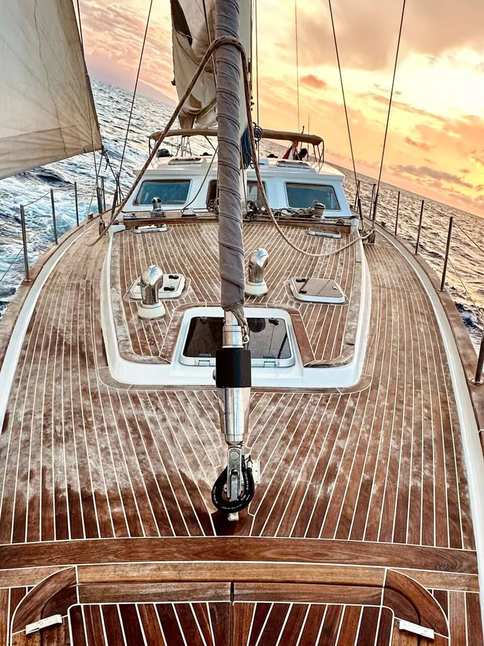 Een zeilboot met een houten dek vaart op zee, met een deels uitgerold zeil en een mast aan de voorzijde. — CRN 63