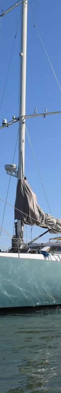 Een lichtgroene zeilboot met opgerolde zeilen en een ankerketting hangt in helder water onder een blauwe lucht, met andere…