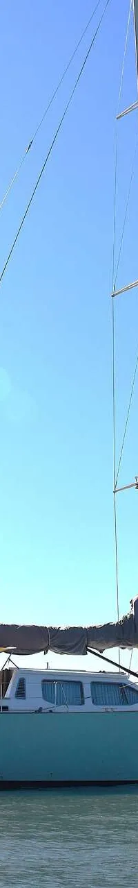 Een lichtblauwe zeilboot met de naam "mahi mahi" op de romp ligt op het water onder een heldere hemel. — CRN 63
