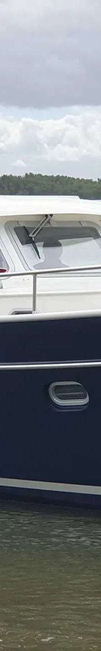 Een donkerblauwe motorboot met een witte opbouw en de naam "GRETHE" op de spiegel, vaart op water.