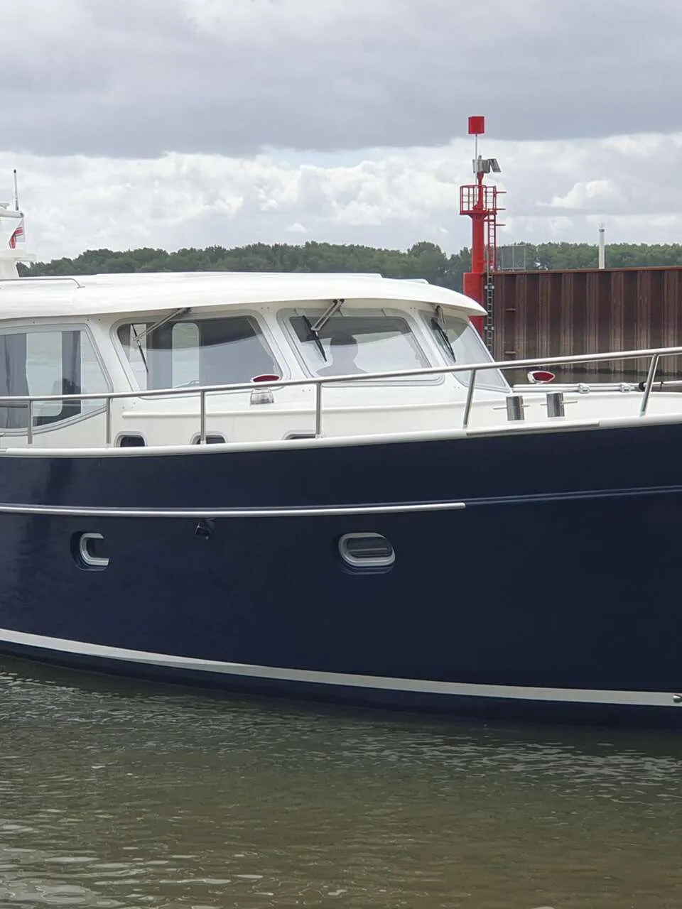 Een donkerblauwe motorboot met een witte opbouw en de naam "GRETHE" op de spiegel, vaart op water.