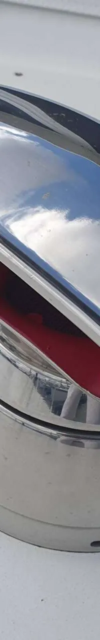 Een close-up van een glimmend metalen ventilatierooster met rode binnenkant op een wit oppervlak.