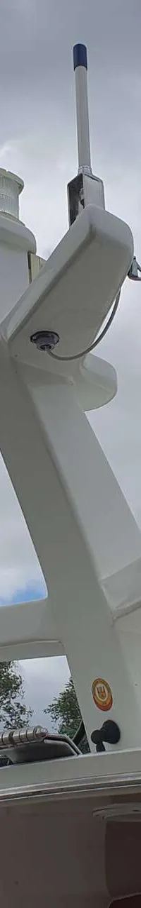 De foto toont een deel van de mast van een boot met navigatieverlichting, antennes en een vlag, tegen een bewolkte lucht.