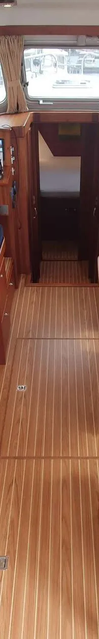 De foto toont het interieur van een boot met een kombuis, stuurstand, zithoek en houten vloer. — Brandsma Noordzeekotter 38