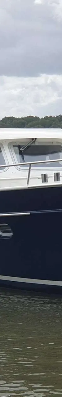 Een donkerblauwe motorboot met witte opbouw en reling vaart op het water, met een rode en groene boei op de achtergrond.