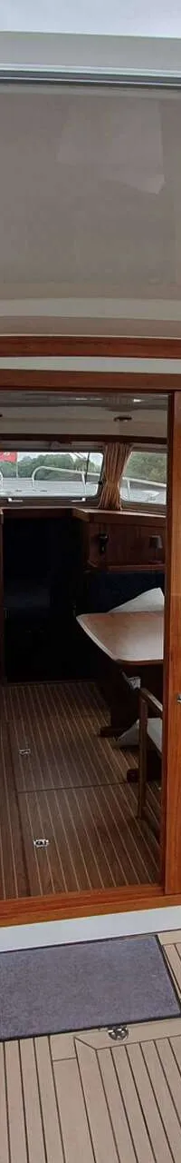 Een achterdek van een boot met twee banken met blauw-wit gestreepte kussens, een houten vloer en een open kajuitdeur.