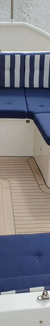 Een bootdek met teakhouten vloer, blauw-wit gestreepte kussens en een Duitse vlag.