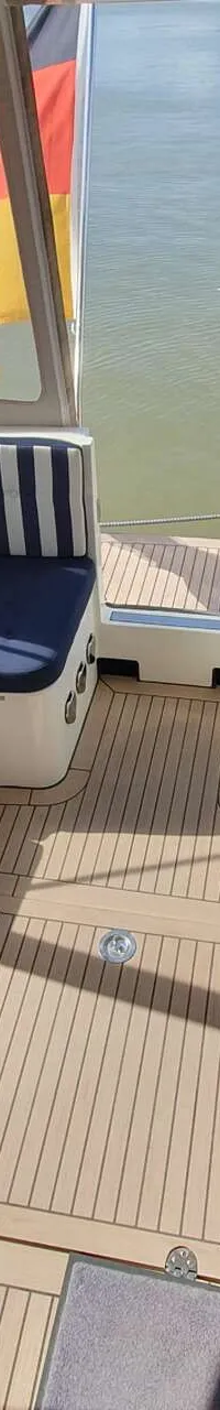 Een bootdek met houten vloer en twee blauw-wit gestreepte banken, met uitzicht op water en een Duitse vlag.