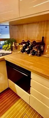 Een moderne kombuis met een aanrechtblad van licht hout, een spoelbak, kookplaat, en diverse flessen en glazen.