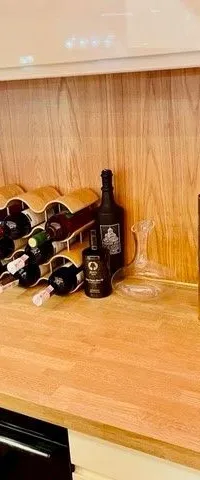 Een houten aanrechtblad met een wijnrek, flessen wijn, sterke drank, een karaf, een cocktailshaker en een koffiezetapparaat.