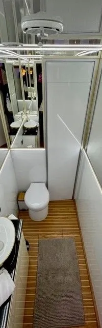 Een interieur met twee toiletten, een wastafel en een spiegelwand, met een houten vloer en een grijze mat.