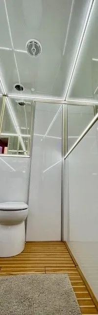 Een interieurfoto van een badkamer met een toilet, houten vloer, witte muren en plafond met verlichting.