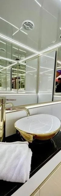 Een badkamer met een gouden kraan, een witte waskom met gouden rand, een handdoek, een zeepdispenser en een toilet.