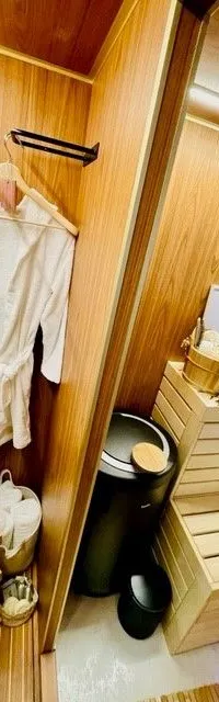 Een houten interieur met een witte badjas aan een hanger, een houten rekje met toiletartikelen en een sauna-achtige bank.