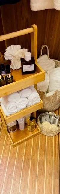 Een houten rek met toiletartikelen en handdoeken staat op een gestreepte houten vloer, omringd door houten wanden.