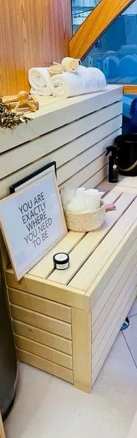Een interieur met houten banken, manden, handdoeken en een zwarte emmer, met een raam op de achtergrond.