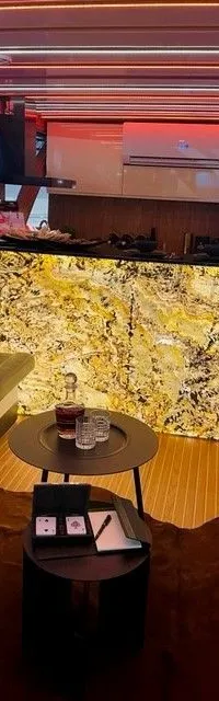 Een interieur van een boot met een zwarte bank, twee ronde tafels, een verlichte bar en een houten vloer.