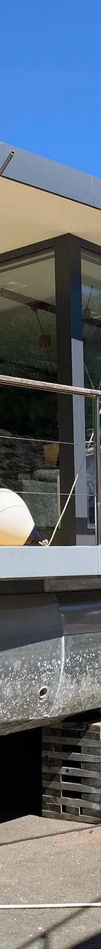 Een moderne woonboot met grote ramen en een plat dak staat op houten blokken op de wal.